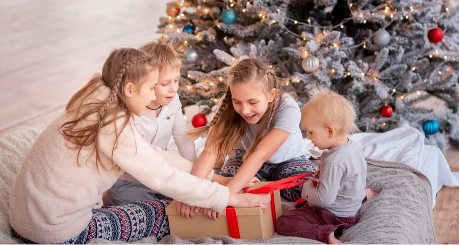 Children opening a present near a Christmas tree.